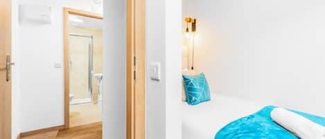 Habitación de hotel con piso de madera, una cama con una colcha azul, un almoháque azul y una lámpara fijada a la pared.