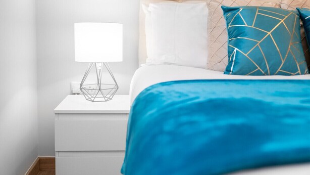 A neatly made bed with a blue blanket, a white pillow, and a decorative pillow with a geometric pattern. - Brand New - Two Bed - Parking - Stourbridge (West Midlands)