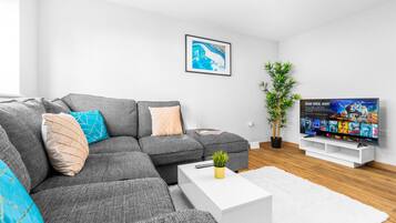 Ein modernes Wohnzimmer mit einem grauen Ecksofa, einem weißen Couchtisch, einem Flachbildfernseher und einer Topfpflanze.