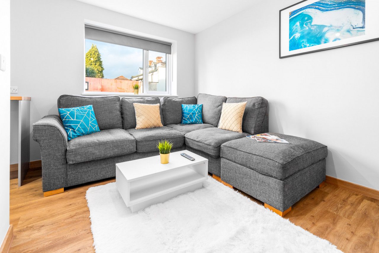 Ein modernes Wohnzimmer mit einem grauen Ecksofa, einem weißen Couchtisch und einem weißen Shaggy-Teppich.