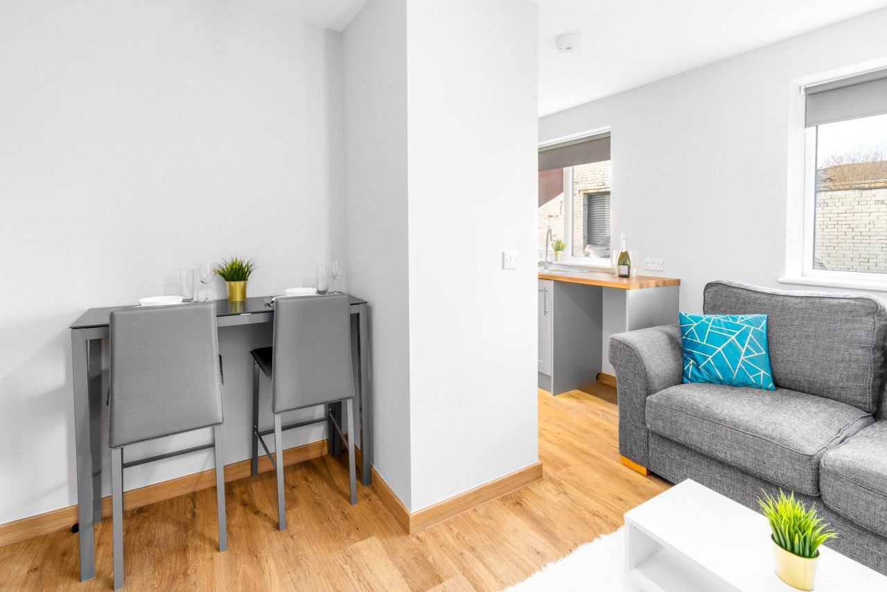 A modern living room with a grey sofa, a white coffee table, and a grey dining table with two chairs.
