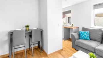A modern living room with a grey sofa, a white coffee table, and a grey dining table with two chairs.