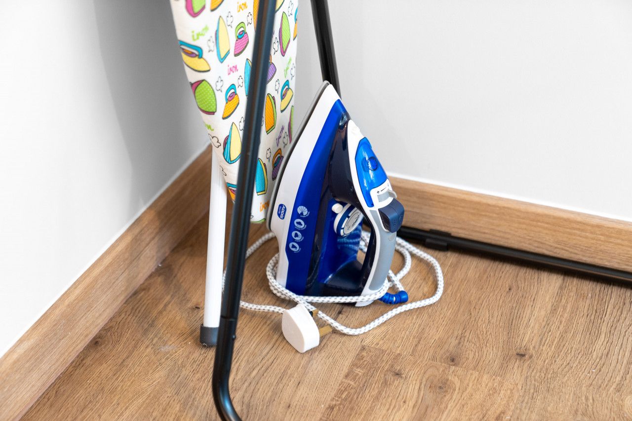 An iron on a wooden floor next to a white wall.