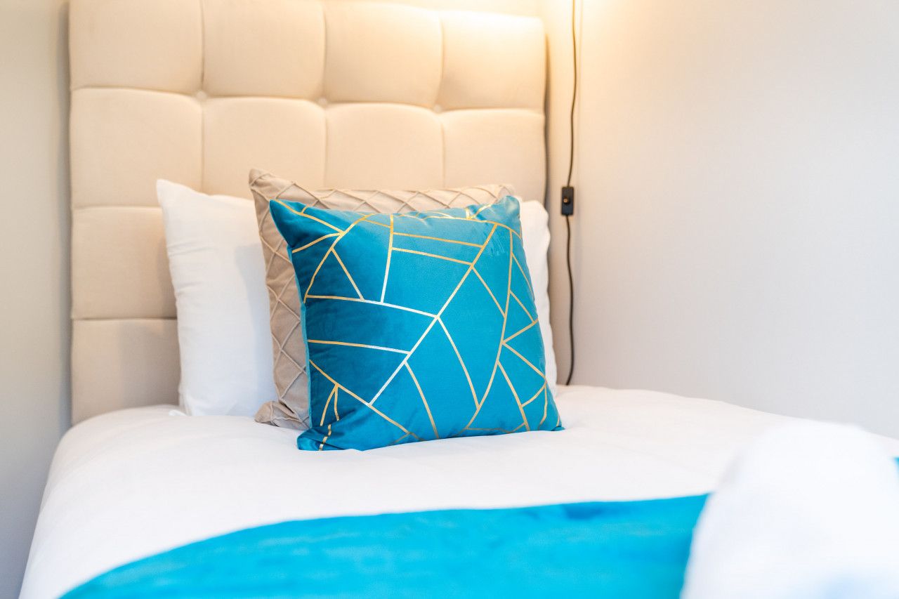 Una cama con cabecera blanca, un almohadón azul con diseño geométrico y un almohadón blanco.