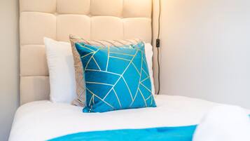 Una cama con cabecera blanca, un almohadón azul con diseño geométrico y un almohadón blanco.