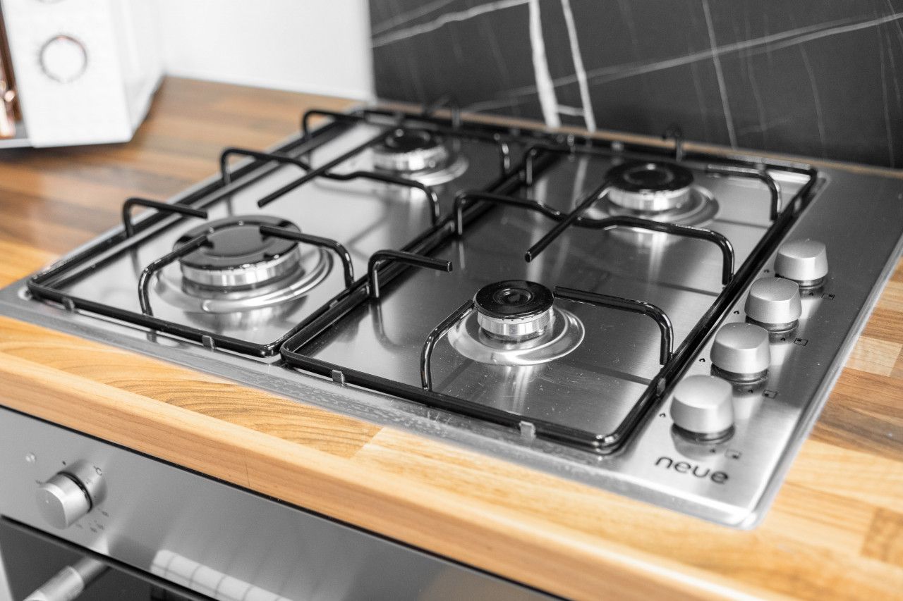 A modern kitchen with a stainless steel gas stove, wooden countertop, and a white appliance in the background.
