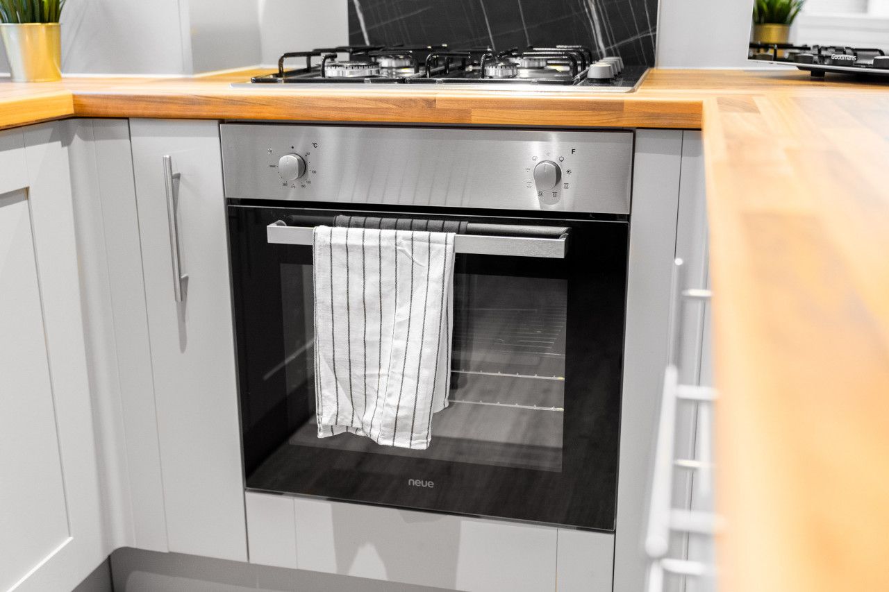 Cocina compacta con horno integrado, extractor de acero inoxidable y encimera de madera.