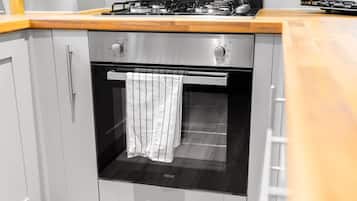 Cocina compacta con horno integrado, extractor de acero inoxidable y encimera de madera.