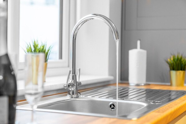 A modern kitchen with a stainless steel sink, a faucet, and a window with plants.