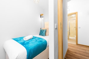 A bedroom with a bed, a bedside lamp, and a view of a bathroom. - Stylish Two Bed - Two Parking Spaces - Stourbridge (West Midlands)