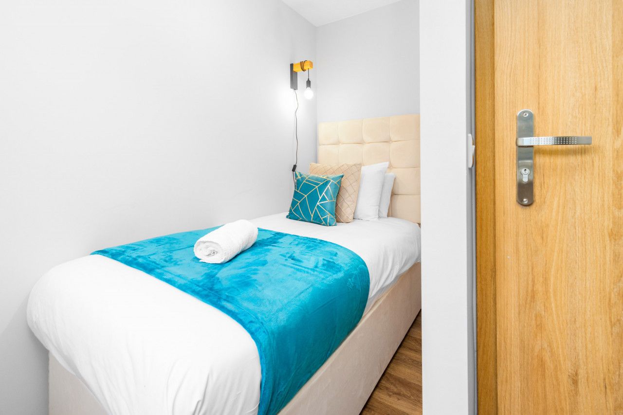 A neatly made bed with a white and blue bedspread, a teal throw blanket, and a white towel.