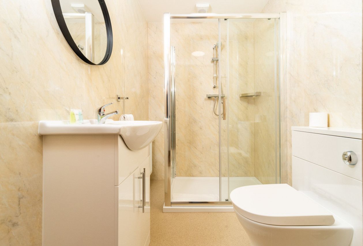 Ein modernes Badezimmer mit einer gläsernen Dusche, einem weißen Waschbecken und einer Toilette.