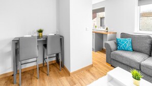 A modern living room with a grey sofa, a white coffee table, and a grey dining table with two chairs. - Brand New Apartment - Parking - Stourbridge (Stourbridge)