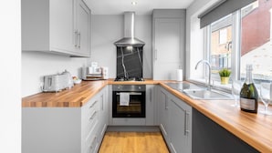 Una cocina moderna con armarios grises, encimera de madera, horno empotrado, campana de acero inoxidable y ventana con vista a la calle.