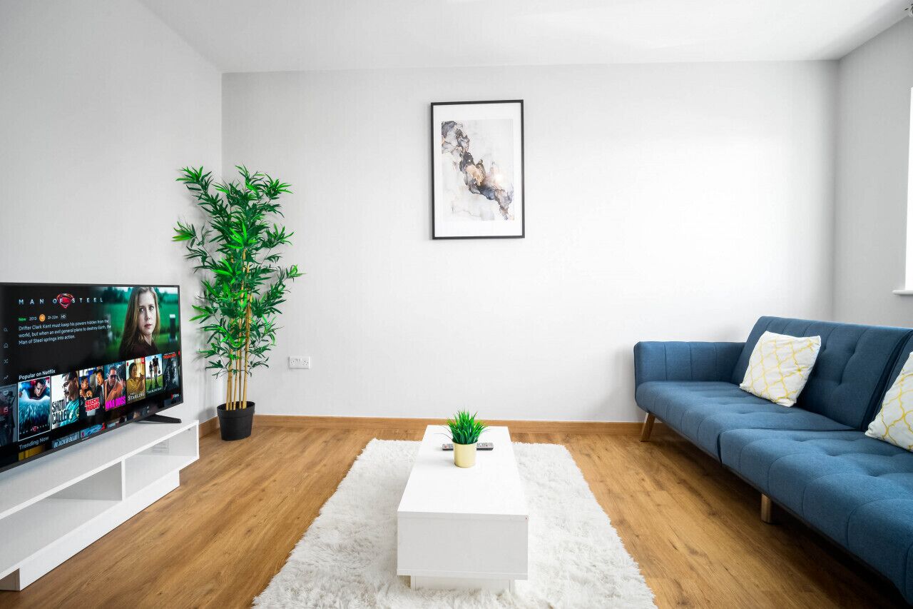 A modern living room with a flat-screen TV, a blue sofa, a white coffee table, and a potted plant.
