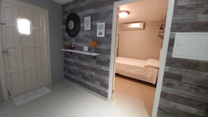 A bedroom with a bed, a white door, a shelf with a vase, and a wall with a circular decoration. - Cozy & Modern (Willemstad)