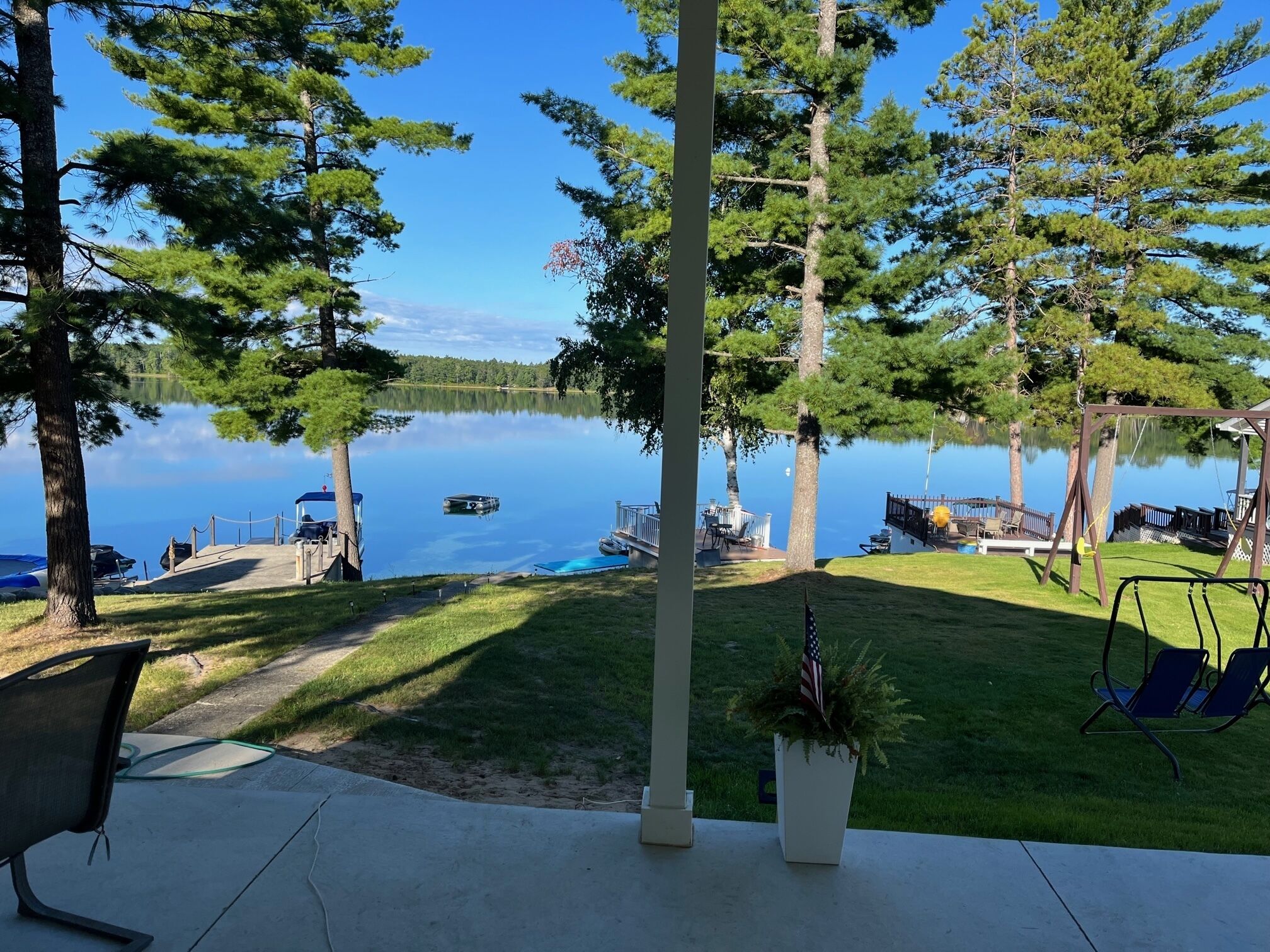 A lakeside deck with a swing set, a small boat docked, and a view of the lake.