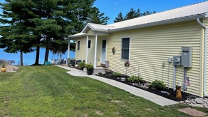 Une maison mobile de plain-pied dotée d’un porche couvert, d’un petit jardin agrémenté de plantes en pot et offrant une vue sur un lac.