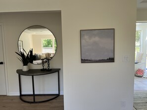A hallway with a round mirror, a console table with a plant, and a framed picture on the wall.