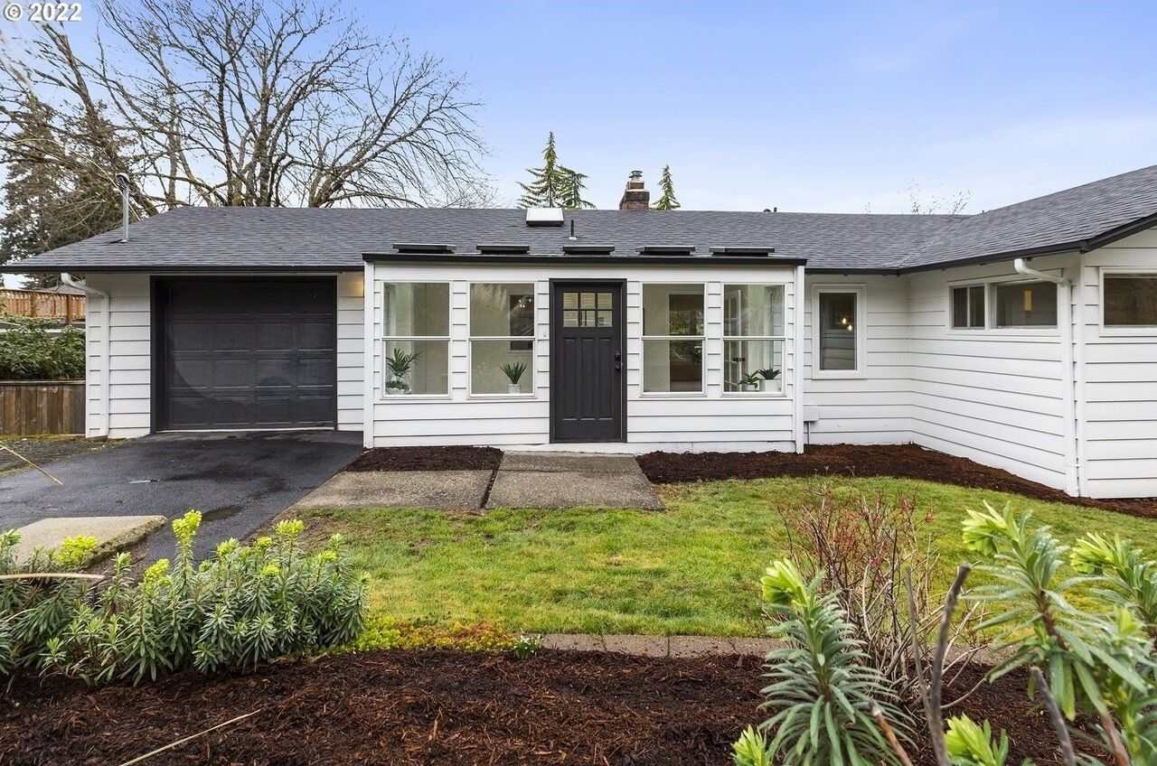 Une maison de plain-pied avec une porte d’entrée noire, un revêtement extérieur blanc et un garage.