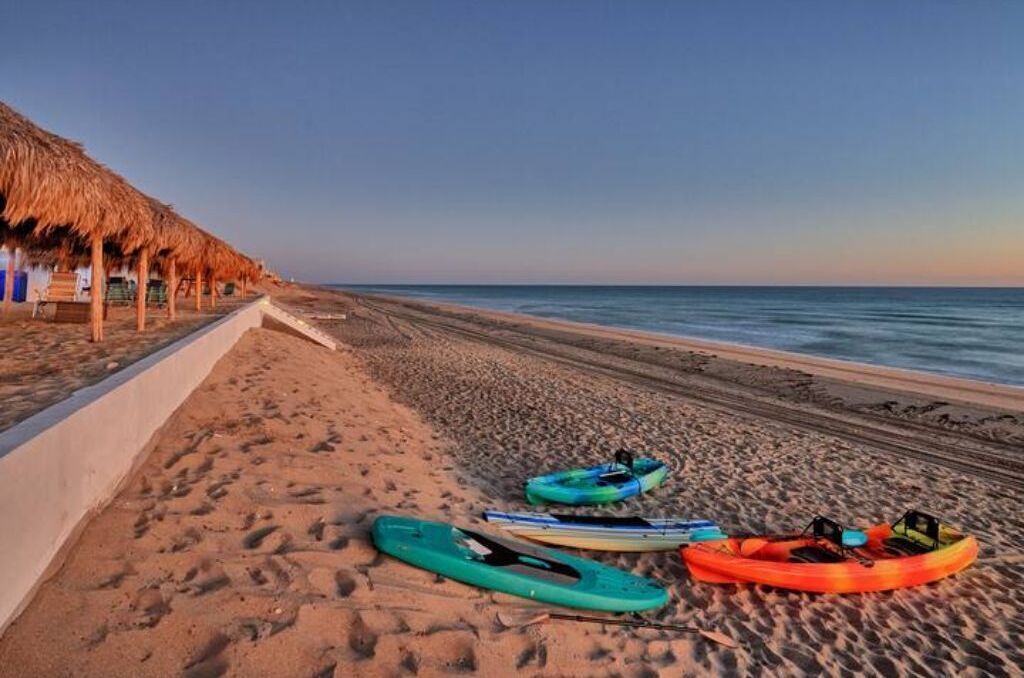 Une plage où l’on peut faire du kayak, avec des kayaks alignés et une structure recouverte d’un toit de chaume.