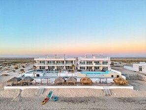 A modern hotel with a pool, multiple balconies, and a desert landscape.