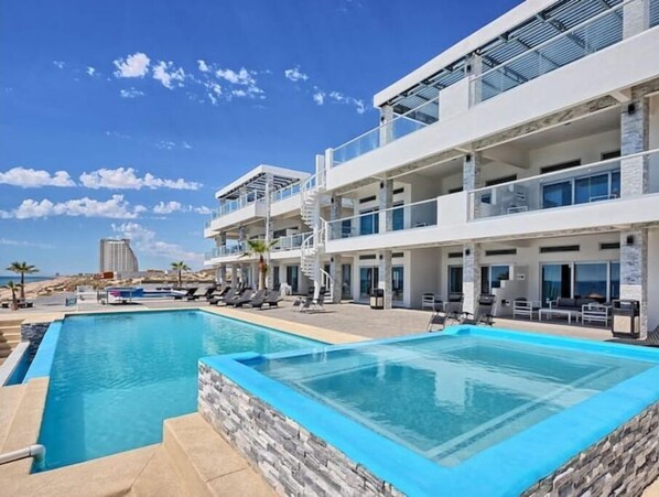 A modern hotel with a pool area, multiple balconies, and a view of the ocean.