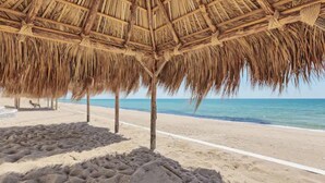 A beach with a thatched roof structure, sandy beach, and clear blue water.