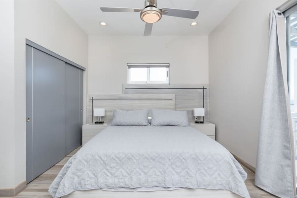 Une chambre à coucher avec un lit, un ventilateur de plafond, une fenêtre et une porte.
