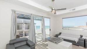 A modern living room with a grey sofa, a white ottoman, and a ceiling fan.