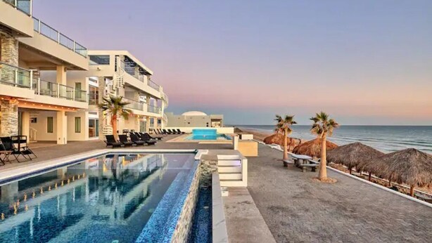 A modern hotel with a pool, beachside seating, and a view of the sea.