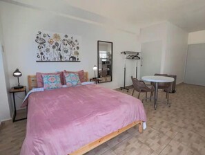 Un dormitorio con cama, escritorio, silla, espejo y una obra de arte en la pared.