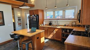 Uma cozinha moderna com armários de madeira, uma ilha central com um laptop, uma geladeira, uma pia e um fogão.