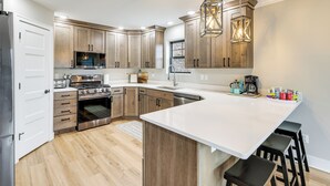 Una cocina moderna con armarios de madera, una isla central, electrodomésticos de acero inoxidable e iluminación colgante.