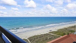 A beach view with a clear sky, a sandy shore, and a building with a red roof. - MVG 1416 Ocean View Penthouse (North Myrtle Beach)