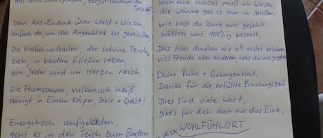 Ein handgeschriebener Zettel mit deutschem Text, vermutlich ein Eintrag aus einem Gästebuch, auf liniertem Papier, platziert auf einem Stuhl.