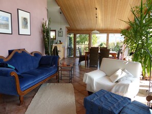Ein Wohnzimmer mit einem blauen Sofa, einem weißen Sofa und einem blauen Sessel. Das Zimmer hat eine Holzbalkendecke und ein großes Fenster.