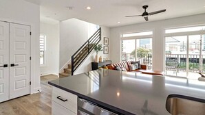 A modern kitchen with a large island, a dining area with a sofa, and a staircase leading to another level. - Rooftop Deck and Ocean Views with VB Local Life! (Virginia Beach)