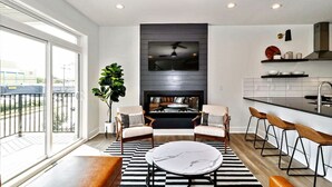 A modern living room with a fireplace, seating area, and a kitchen with bar stools. - Rooftop Deck and Ocean Views with VB Local Life! (Virginia Beach)