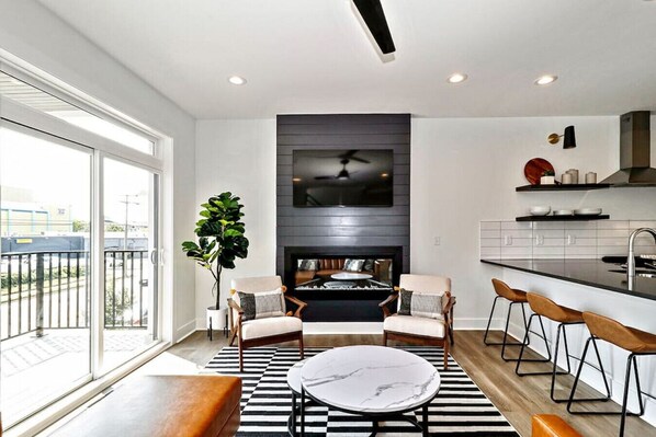 A modern living room with a fireplace, seating area, and a kitchen with bar stools.