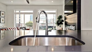 A modern kitchen with a stainless steel sink, large windows, and a view of the city. - Rooftop Deck and Ocean Views with VB Local Life! (Virginia Beach)