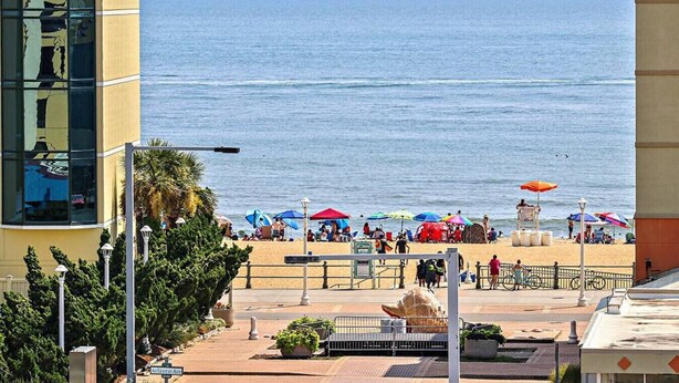 A beach view with umbrellas, a lifeguard tower, and a building with reflective windows. - Rooftop Deck and Ocean Views with VB Local Life! (Virginia Beach)