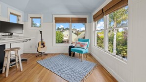 Una cocina con encimera de madera, un taburete, una guitarra y vistas a una casa a través de amplios ventanales.