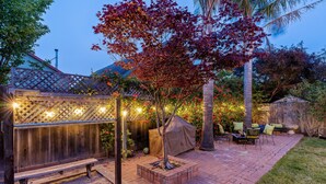Un patio con un banco de madera, una zona de estar cubierta y una jardinera de ladrillo con un árbol.