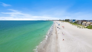 A beach with a long stretch of sand, a few umbrellas, and buildings in the background. - Gulf Views • Heated Spa • Steps to Beach (Treasure Island)