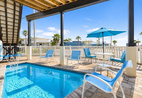 A swimming pool with lounge chairs and umbrellas, surrounded by a white fence and palm trees. - Gulf Views • Heated Spa • Steps to Beach (Treasure Island)