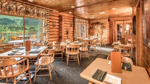 A log cabin-style restaurant with wooden furniture, large windows offering a view of the forest, and a cozy interior. - Kenai Princess Wilderness Lodge (Cooper Landing)