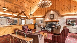 A log cabin-style interior with a registration desk, seating area, fireplace, and a chandelier. - Kenai Princess Wilderness Lodge (Cooper Landing)
