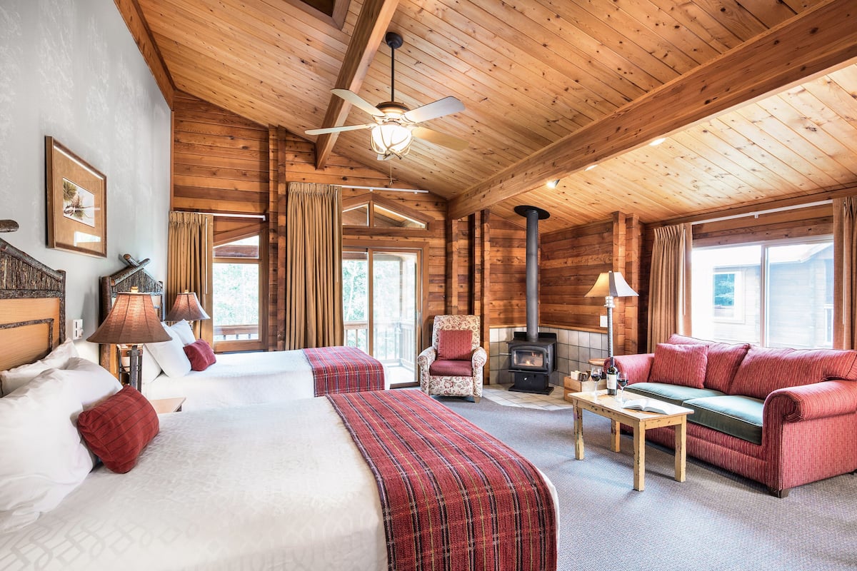 A log cabin room with two beds, a sofa, a table, and a fireplace.