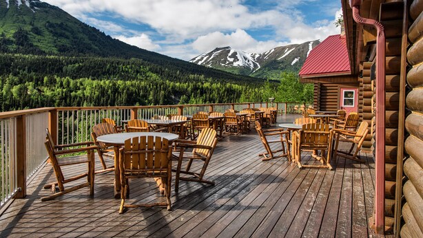 A wooden deck with outdoor seating and a mountain view. - Kenai Princess Wilderness Lodge (Cooper Landing)